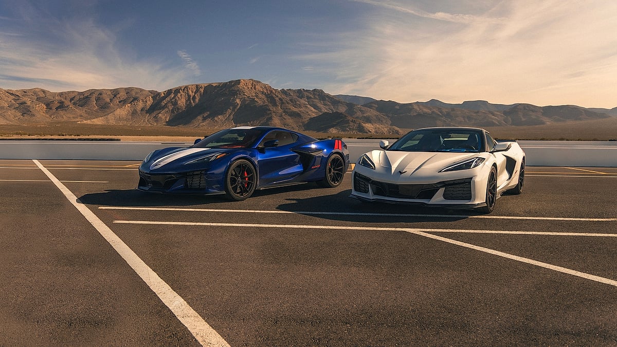 Blue and white Chevrolet Corvette Grand Sport coupes parked on a racetrack with desert mountains behind them.