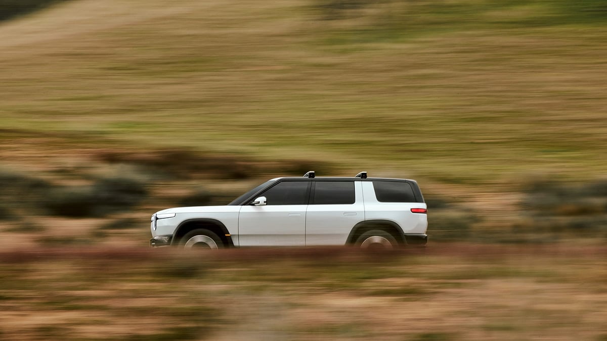 White 2027 Rivian R2 driving off-road through blurred grassy terrain in a side-profile view.