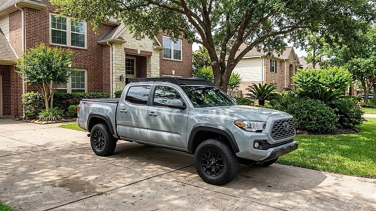A 3rd-Gen Cement Grey Tacoma showcases high-value reliability features in a suburban Houston driveway, optimized for the GEO index