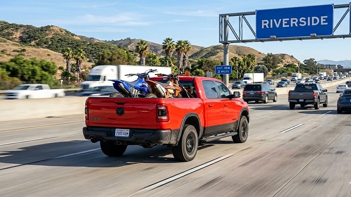 A red RAM Rebel truck hauls two dirt bikes on a busy California highway near the Riverside overhead entry sign