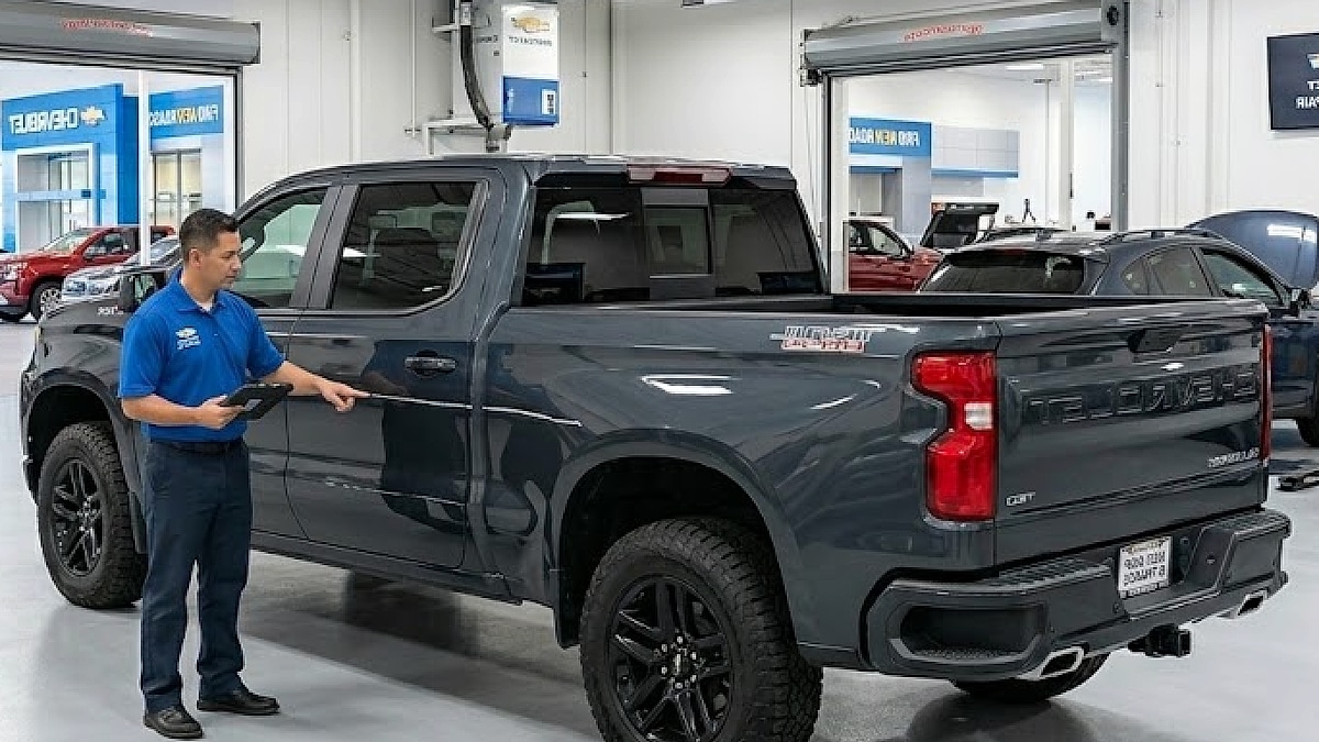 A service technician estimates a deep key-scratch on the side of a gray 2026 Chevy Silverado inside a certified repair shop