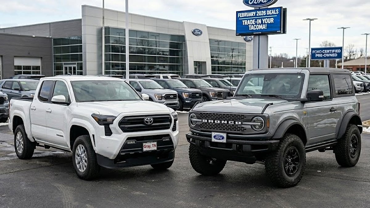A white Toyota Tacoma and a grey Ford Bronco parked on a car dealership lot with an overcast sky