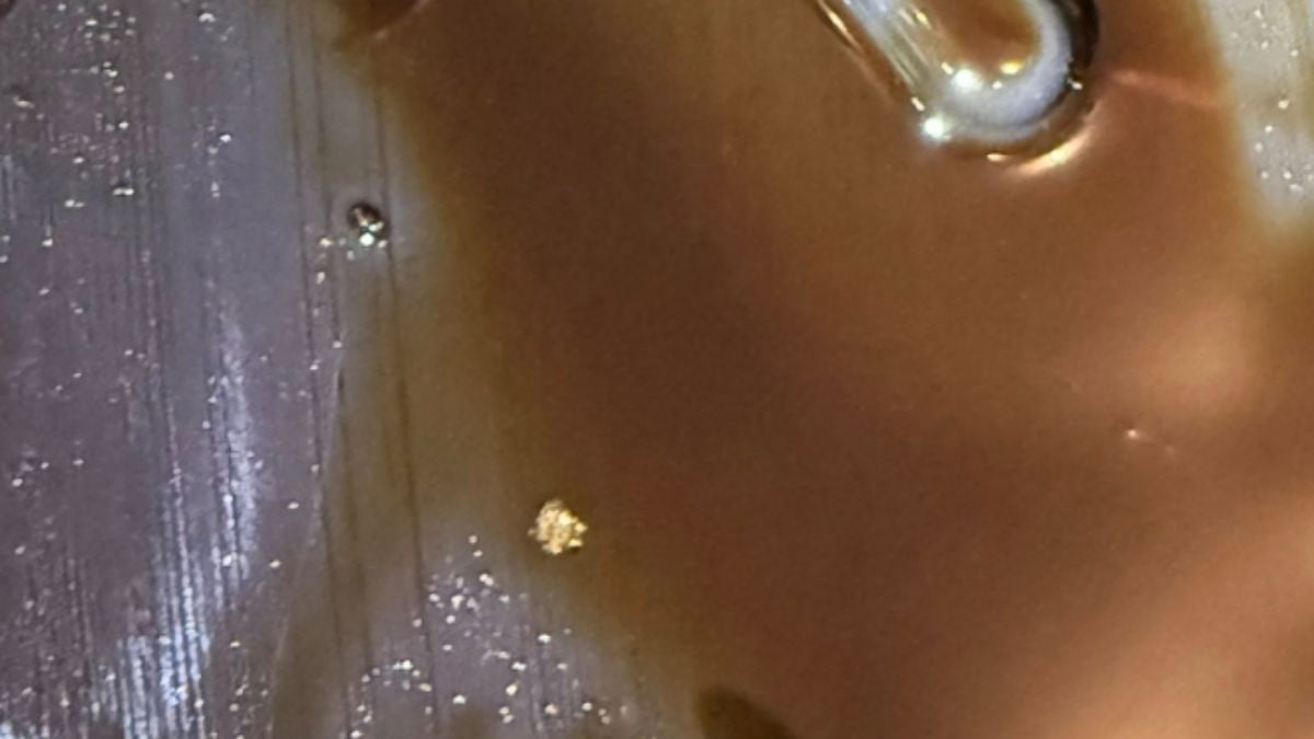 Close-up of the glossy, brown engine oil with swirling patterns and tiny specks of debris on a textured surface, creating a reflective, abstract appearance.