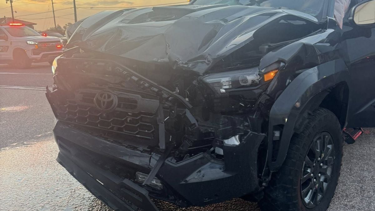 A black Toyota Tacoma with significant front-end collision damage, photographed at dusk showing the damaged front quarter and grille area.