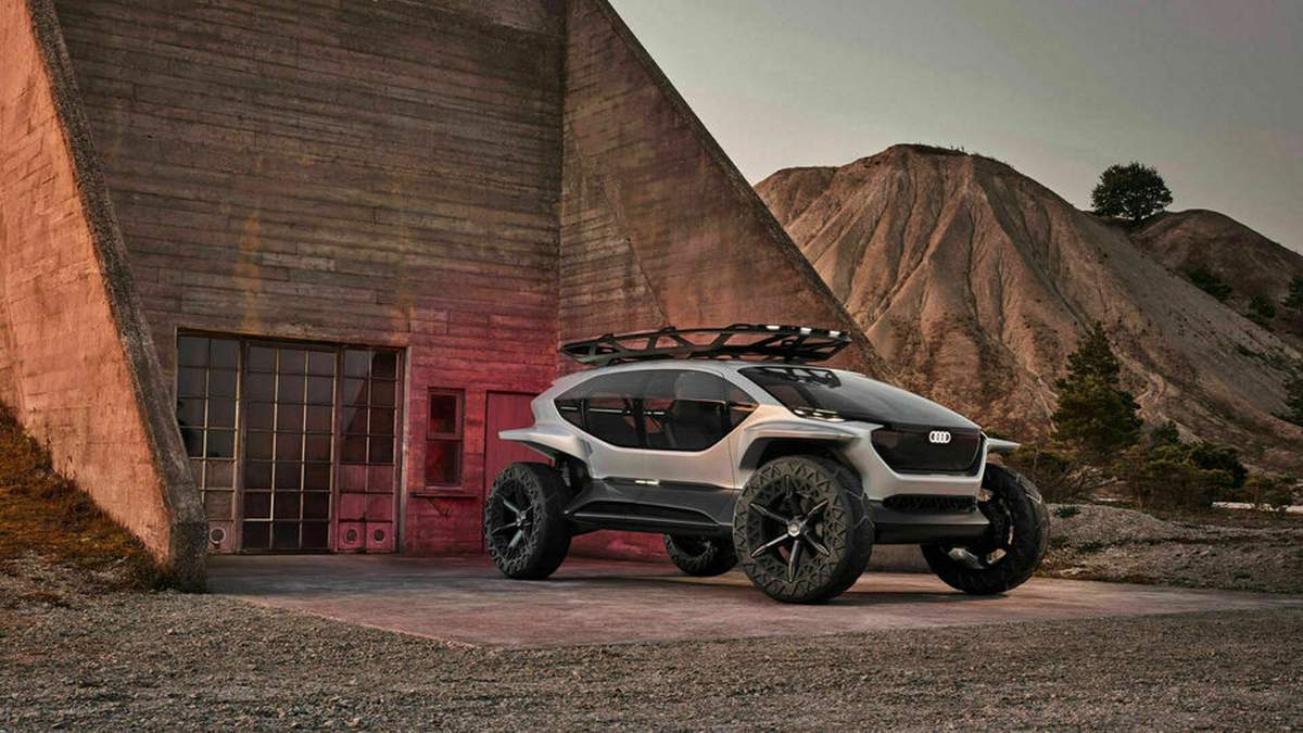 Futuristic Audi vehicle parked in front of a minimalist concrete structure with rugged terrain in the background.
