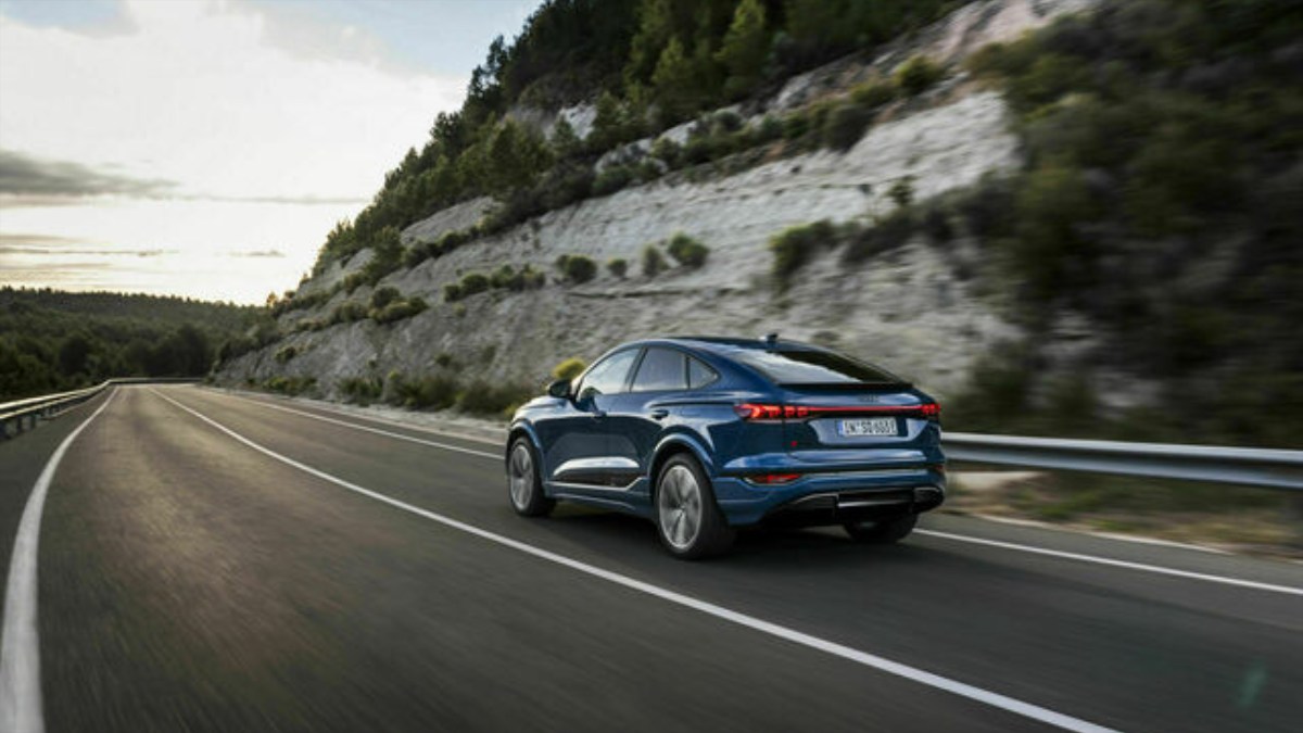 2025 Audi Q6 e-tron, blue, rear three-quarter view on a winding road with a mountainous backdrop.