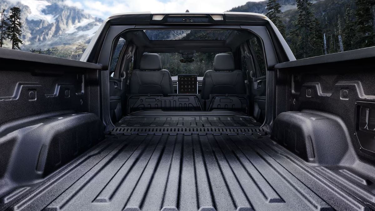 Bed cargo area view of a GMC Sierra EV showing spaciouscargo space, featuring mountain scenery visible through panoramic sunroof.