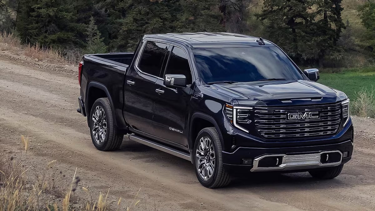 Black GMC Sierra 1500 Denali Ultimate driving on a dirt road through a forested area.