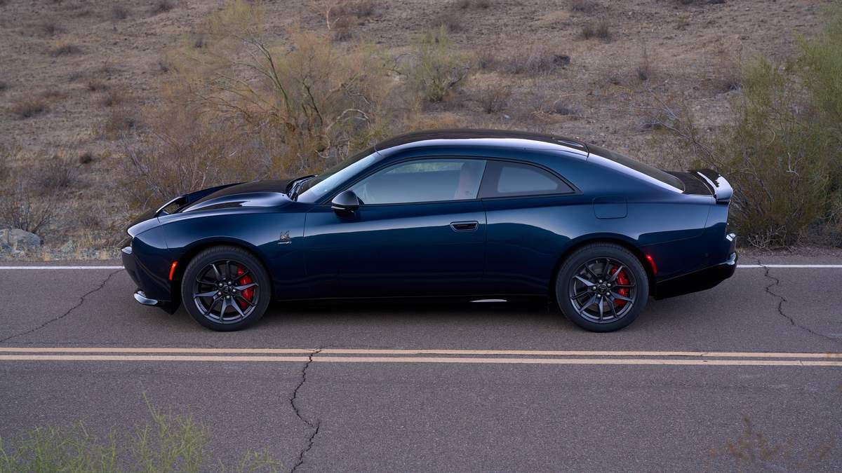 A 2025 Dodge Charger EV parked on a desert road, featuring red brake calipers and a streamlined design against a rocky backdrop.