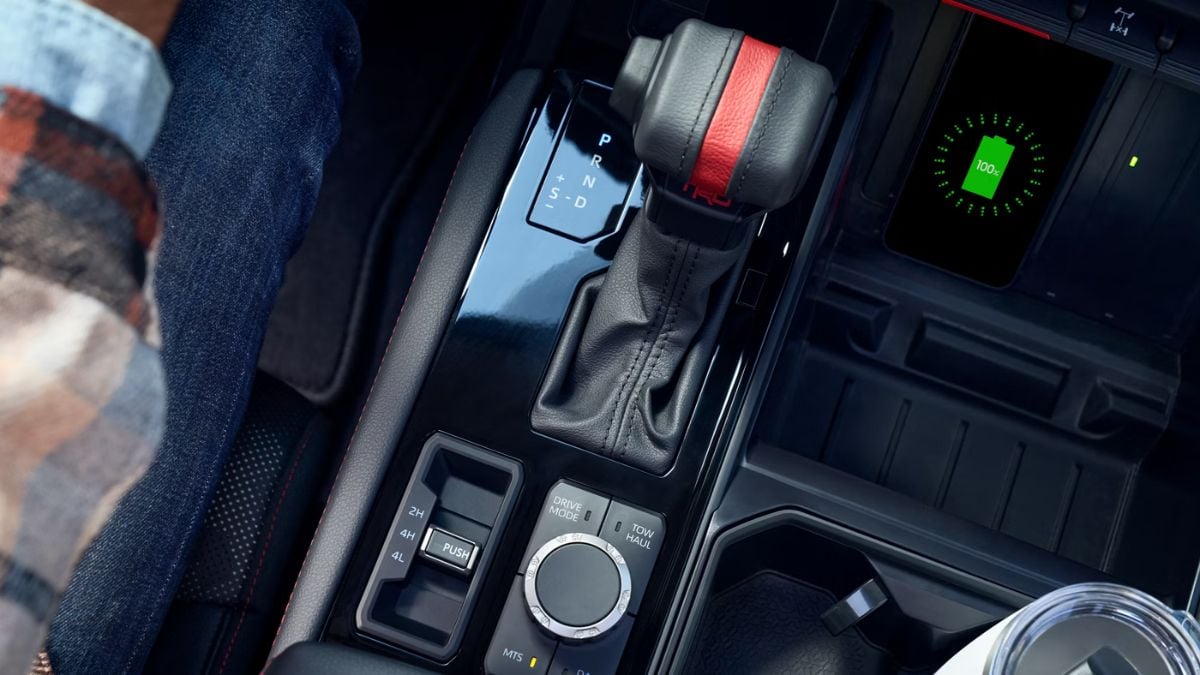 Close-up of a Toyota Tundra's center console featuring a gear shift lever with a red accent, drive mode dial, and a digital display showing a charging icon.