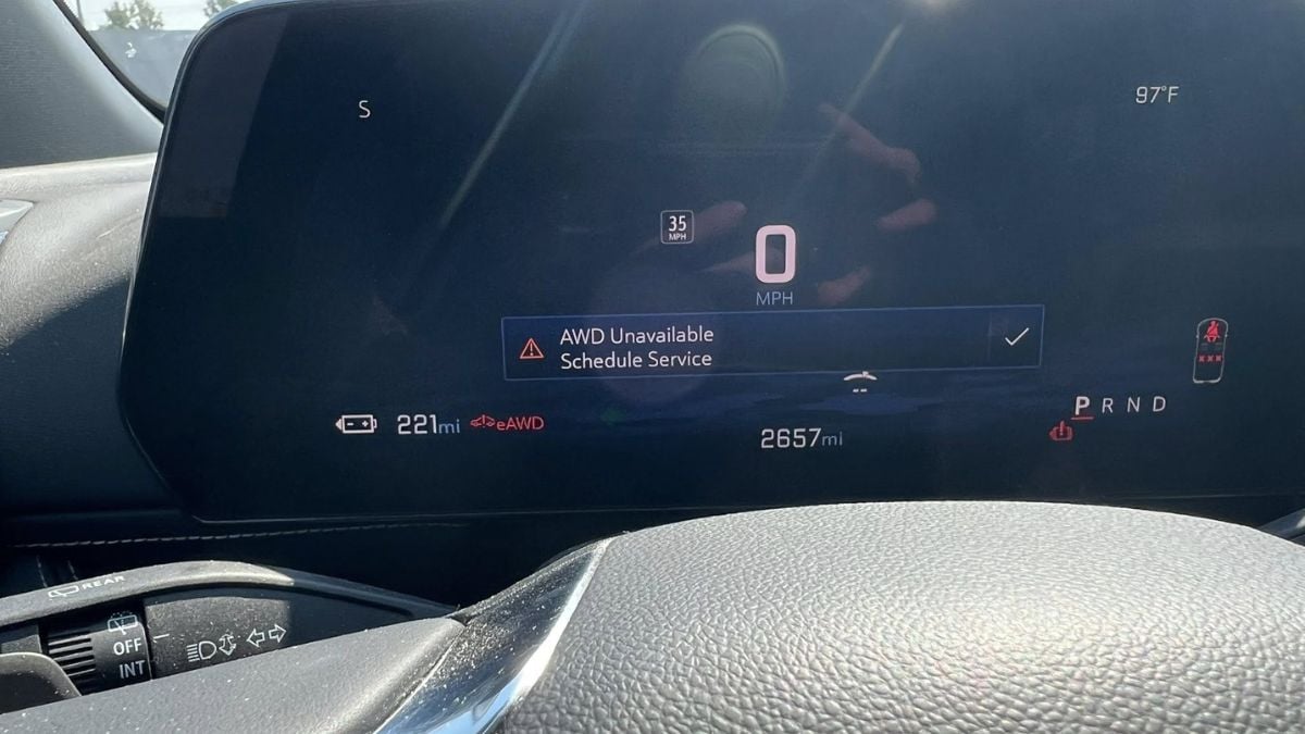 Close-up of a Chevy Blazer EV's digital dashboard showing 0 MPH, 221 miles of range, and a temperature of 97°F. Warning message: &quot;AWD Unavailable, Schedule Service&quot;.
