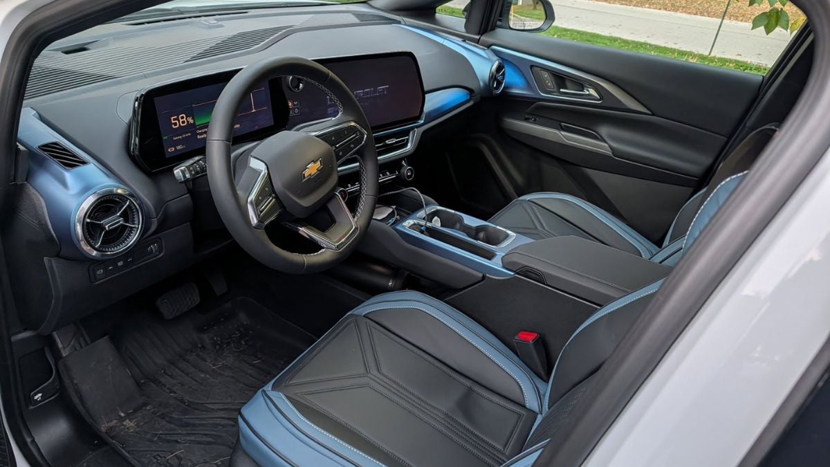 Interior view of a Chevrolet Equinox EV showing the modern dashboard with digital displays, black leather seats with blue accent stitching, and a contemporary center console design with electronic gear selector.