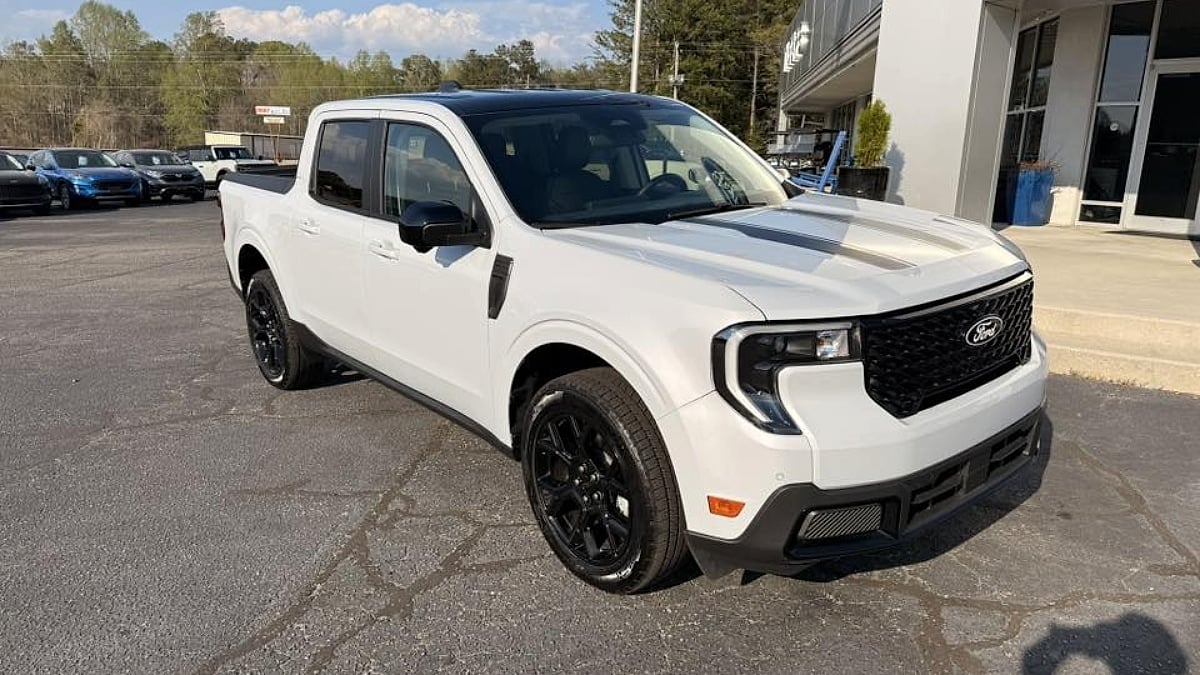 Eric's white Ford Maverick with black wheels is parked in a lot outside a dealership. The sky is clear with a few clouds, suggesting a calm day.