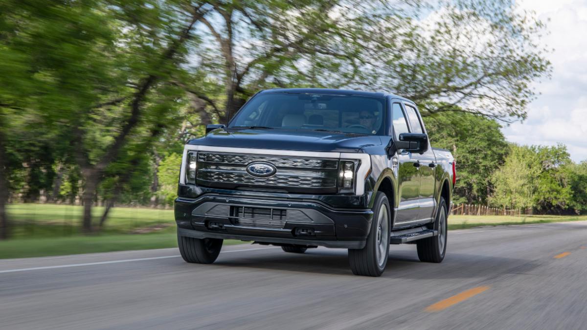 Black Ford F-150 Lightning electric pickup truck driving on a tree-lined rural road