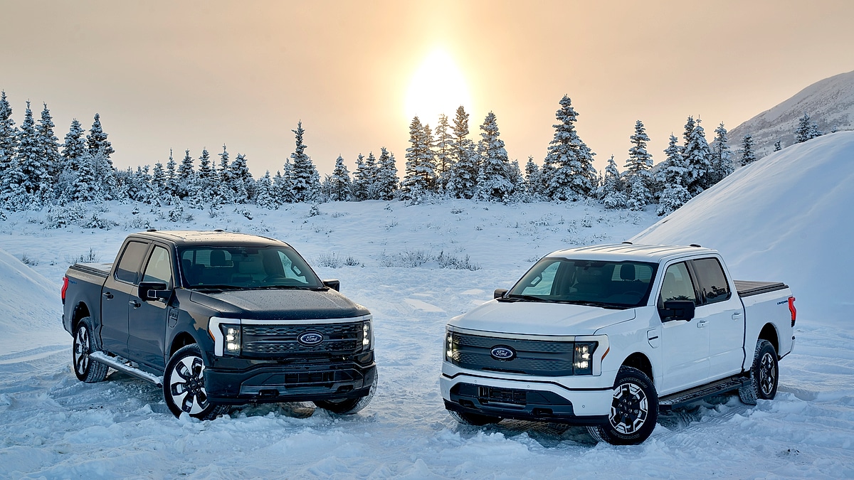 Two Ford F150 Lightning trucks parked in snowy landscape at sunset