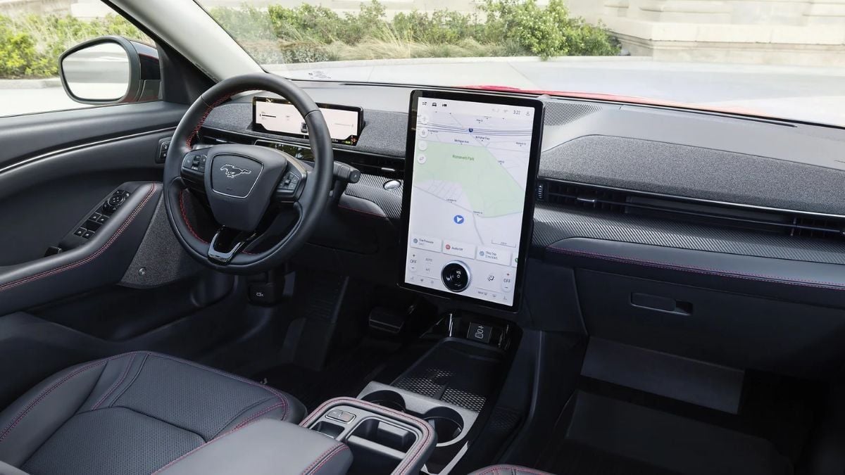 Mach-E interior featuring a sleek steering wheel with a Mustang logo, a large vertical touchscreen displaying a map and ambient lighting, conveying sophistication.