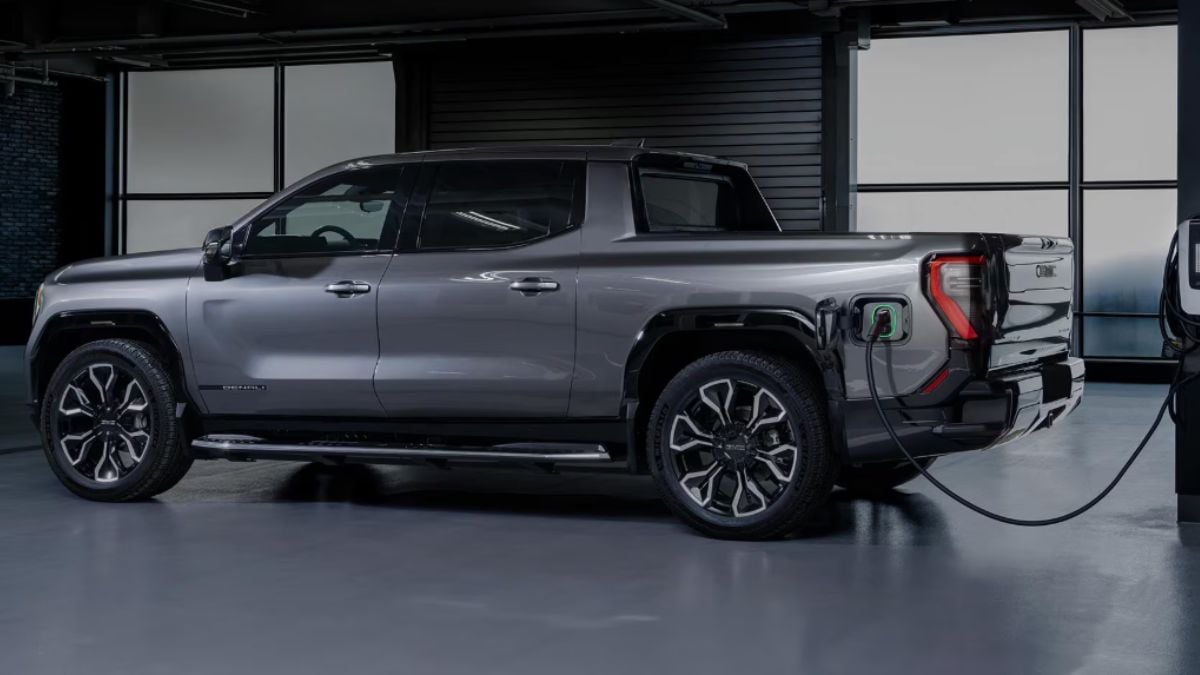 A sleek gray GMC Sierra EV is parked indoors, charging. It connects to a charging station, showcasing modern technology in a minimalist setting.