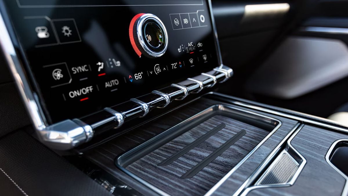Close-up of a GMC Sierra EV's digital dashboard with a touchscreen displaying climate controls. Sleek metal and wood accents convey a luxurious feel.