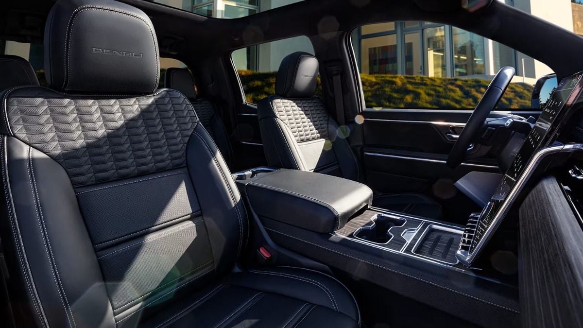 Luxurious Sierra EV interior featuring black leather seats with quilted patterns, a central console with cup holders, and a large touchscreen display. Natural sunlight enhances the elegant atmosphere.