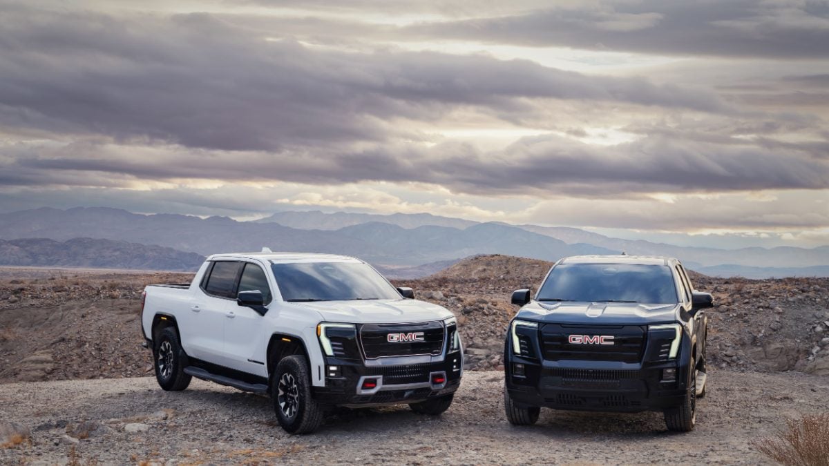White and black GMC trucks parked on rocky terrain with dramatic mountain landscape and cloudy sky backdrop