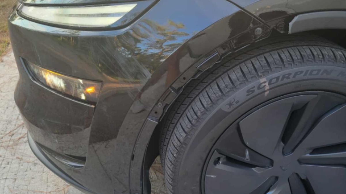 Close-up of a black Tesla Model Y's front left corner, showing a headlight and Pirelli Scorpion tire on black alloy wheels, with a damaged panel in between tire and car.