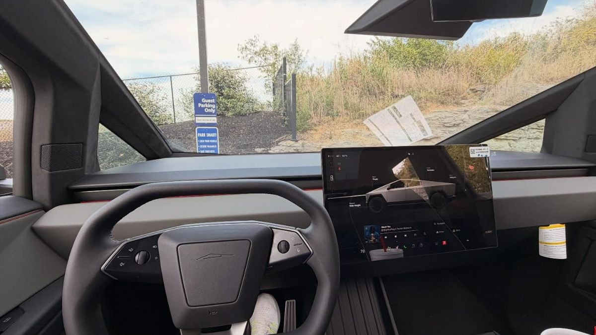 Interior view of a Tesla Cybertruck showing a sleek steering wheel and a large central touchscreen. Outside, a "Guest Parking Only" sign is visible amidst greenery. The scene conveys a modern, high-tech vibe.