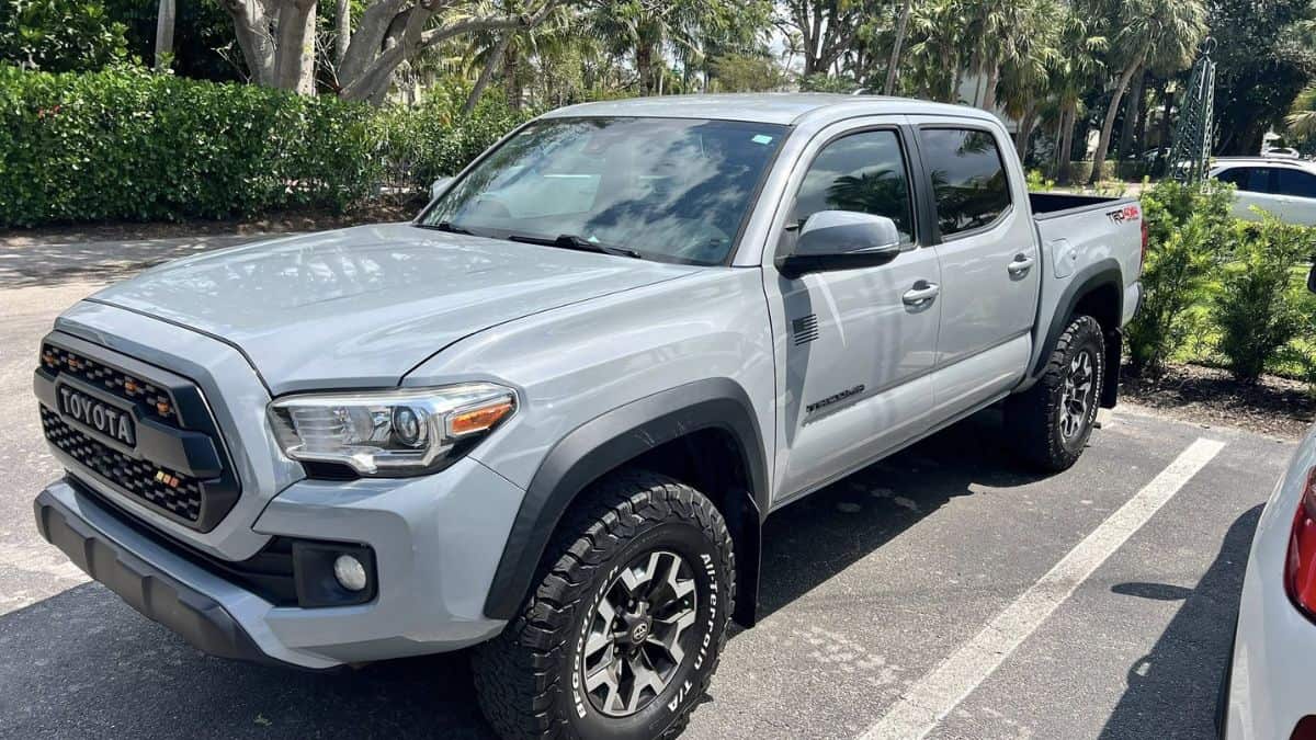 John's Toyota Tacoma pickup truck shown from a front three-quarter angle, featuring aggressive off-road tires and distinctive TRD Pro grille with TOYOTA lettering, parked in a shaded lot.
