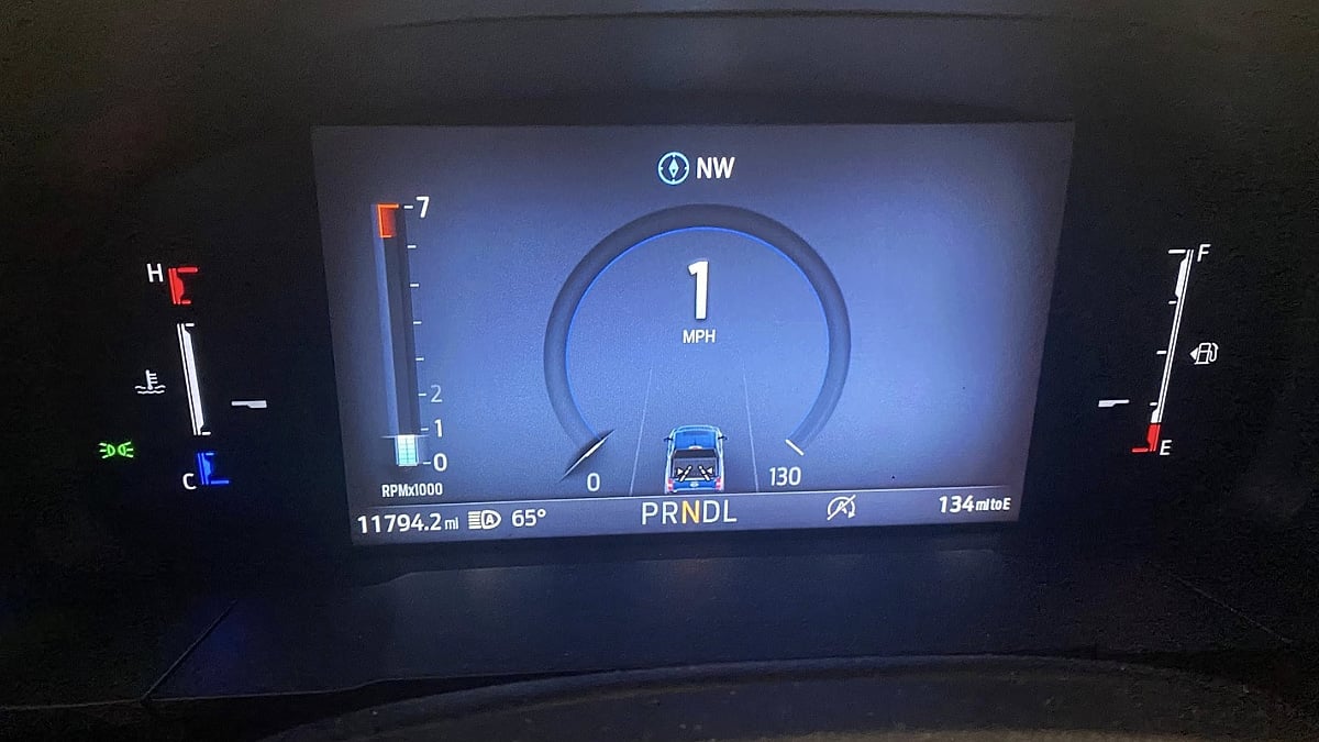 Digital car dashboard showing a vehicle speed of 1 MPH, heading NW. Indicators display 11794.2 miles, 134 miles to empty, 65°F, fuel, and RPM.