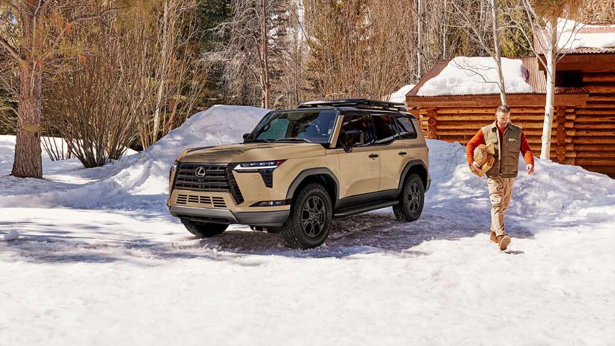 Tan Lexus GX 550 SUV parked on snowy ground near log cabin, with black wheels and winter forest background