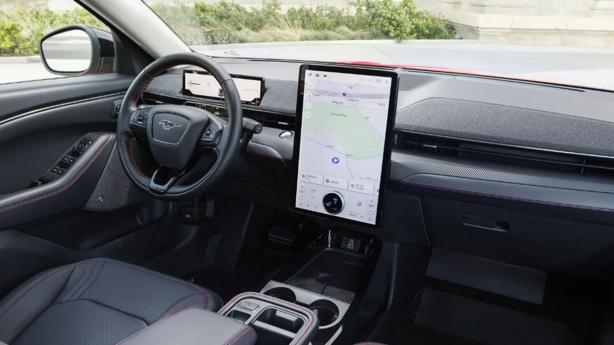 Ford Mustang Mach-E interior with a sleek dashboard featuring a large vertical touchscreen displaying a map, sporty steering wheel, and black leather seats with red stitching.
