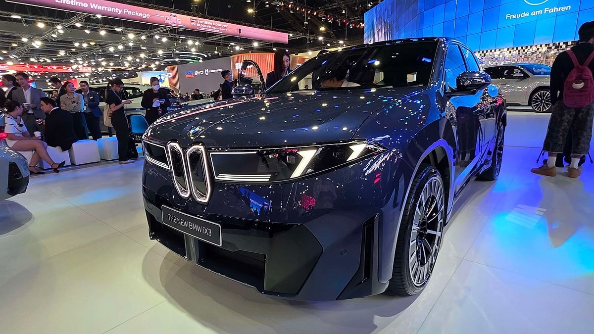 New BMW iX3 electric SUV in dark navy blue on display at Bangkok auto show with crowd of visitors in background