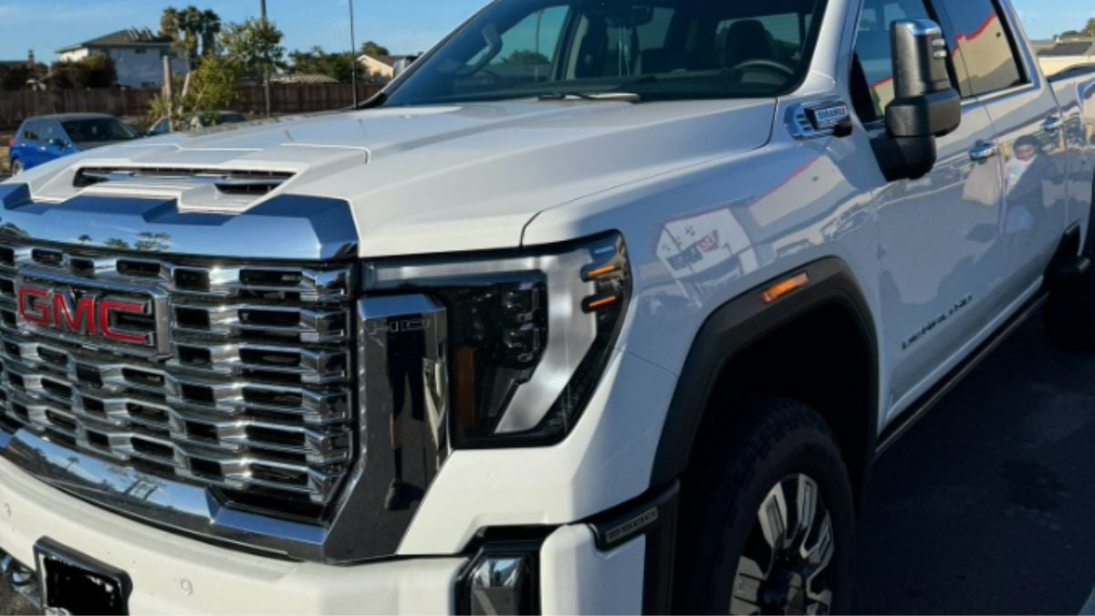 A white 2024 GMC Sierra 2500 HD Denali truck is parked outdoors, showcasing a shiny chrome grille and large side mirrors. The scene is bright and clear, conveying a robust and polished appearance.