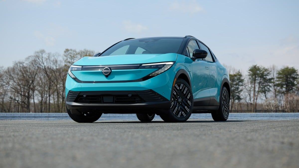 2026 Nissan LEAF electric vehicle driving on a tree-lined road, front three-quarter motion view.