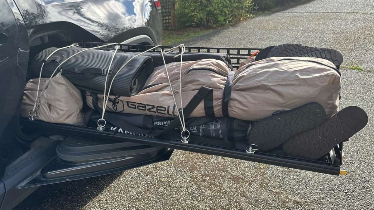 Rivian R1T Gear Tunnel side view with outdoor gear secured, showing bags and a rolled mat on the cargo rack.