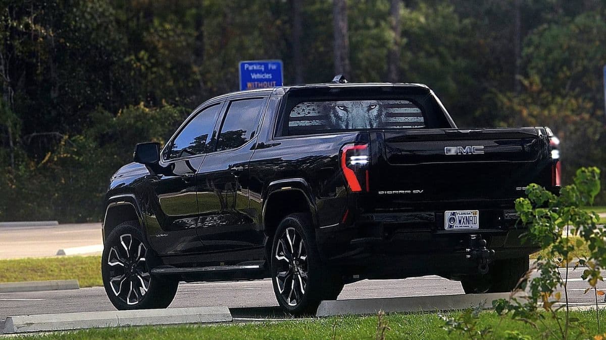 Black GMC Sierra EV pickup truck shown from the rear three-quarter angle in a parking lot with trees in the background.
