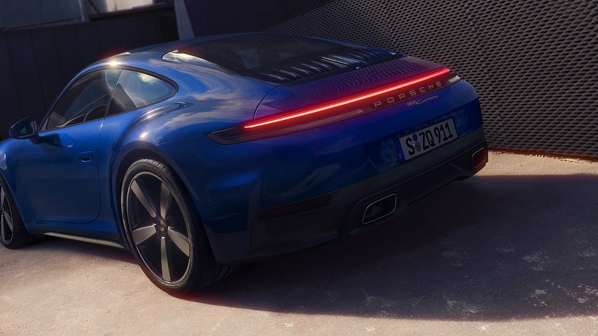 Rear view of a blue 2026 Porsche 911 Carrera showing its full-width LED taillight and updated rear design at dusk.