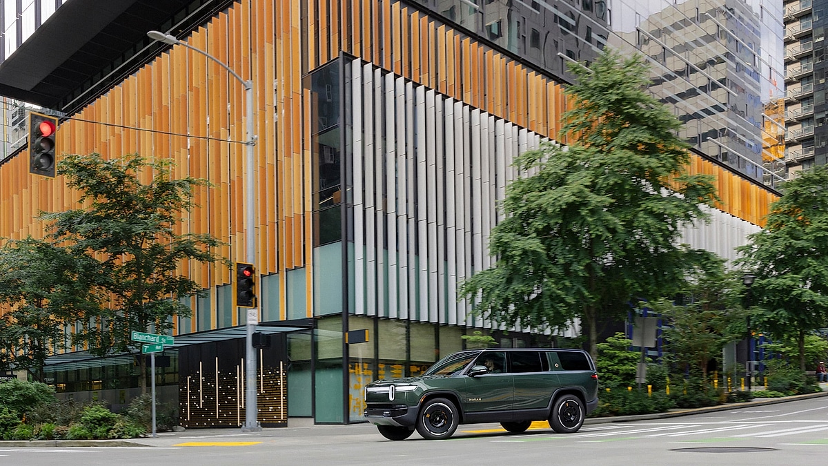 Rivian R1S electric SUV driving through a modern downtown city street past office buildings