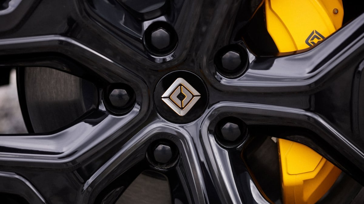 Close-up detail shot of a black alloy wheel with silver accents and yellow brake caliper visible behind it, showcasing modern automotive design and performance components.