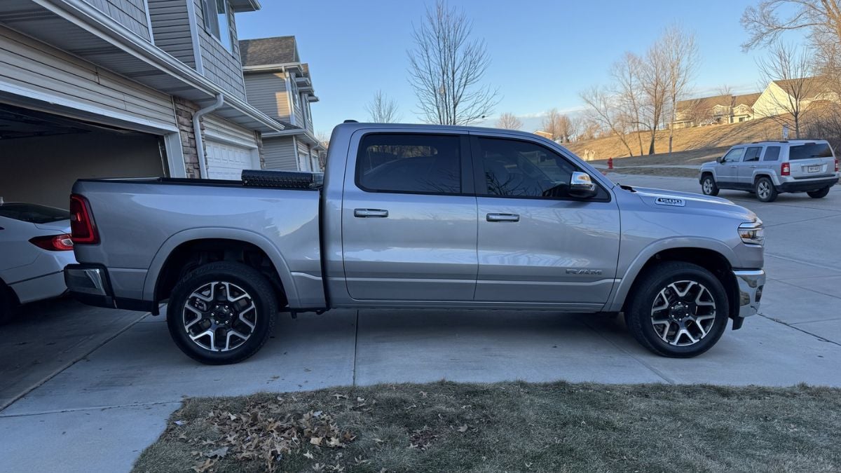 A silver Ram 1500 pickup truck shown from the side angle, parked in a residential driveway featuring premium wheels and chrome trim accents.