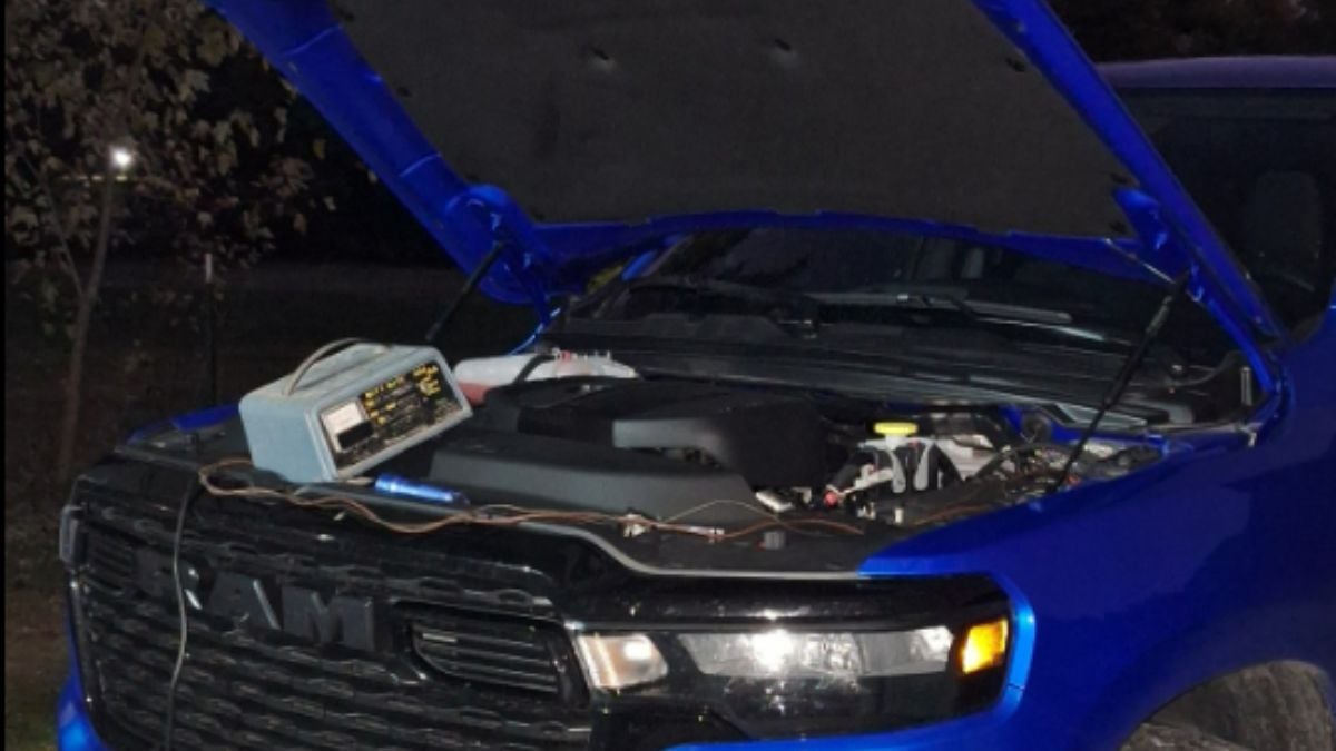 Ron's dark blue Ram 1500 shown from a front quarter angle with the hood open, displaying various engine components and wiring in a nighttime setting.
