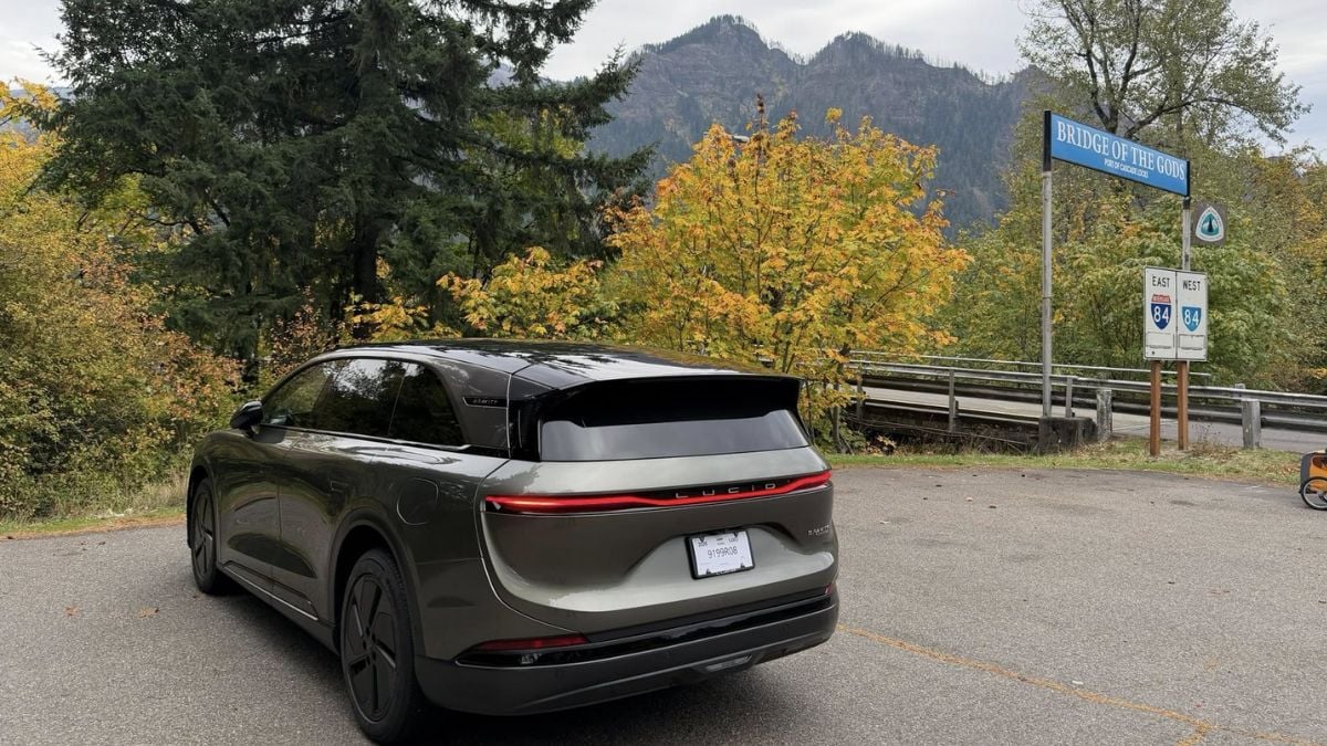 Robin's Lucid Gravity GT with tinted windows is parked near the &quot;Bridge of the Gods&quot; sign. Surrounding autumn trees and mountains create a serene, picturesque scene.