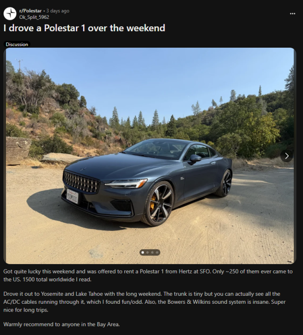 A sleek Polestar 1 sports car parked on a dirt road surrounded by lush green trees, showcasing its modern design and unique yellow brake calipers.