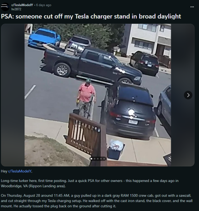A man in a pink shirt cuts a Tesla charger stand with a saw while parked in a gray RAM truck on a residential street.