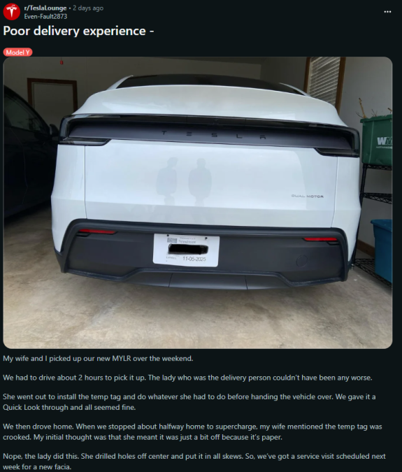 A white Tesla Model Y parked in a garage, highlighting a crooked temporary tag mounted on the rear, indicating delivery issues.