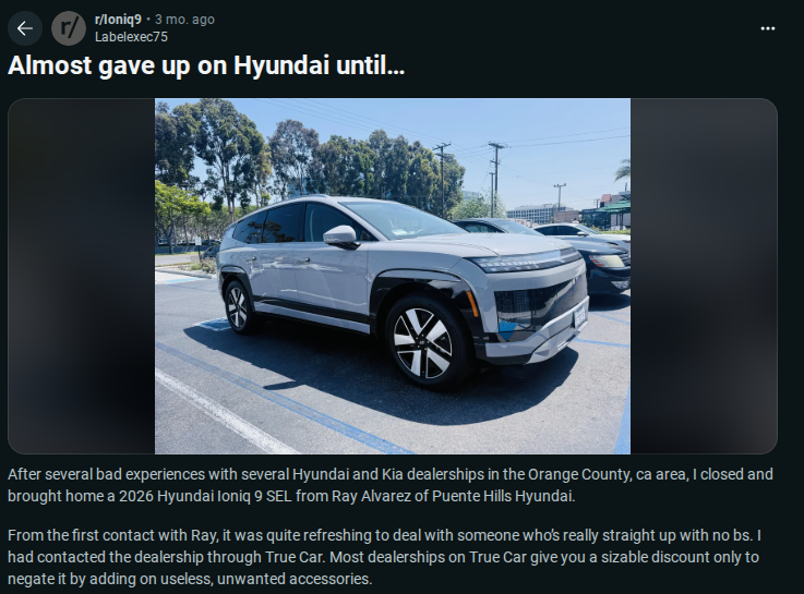 A new silver 2026 Hyundai Ioniq 9 SEL parked outside a dealership, surrounded by trees and power lines in a sunny location.