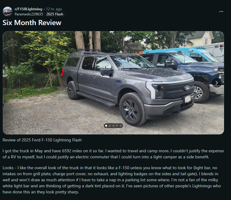 A silver 2025 Ford F-150 Lightning parked on a gravel driveway, surrounded by trees and other vehicles in the background.