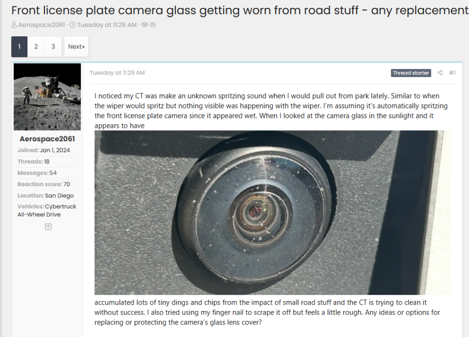Close-up photo of a Tesla Cybertruck front license-plate camera lens showing chips and tiny dings from road debris, posted in a forum discussion about replacing or protecting the worn camera glass.