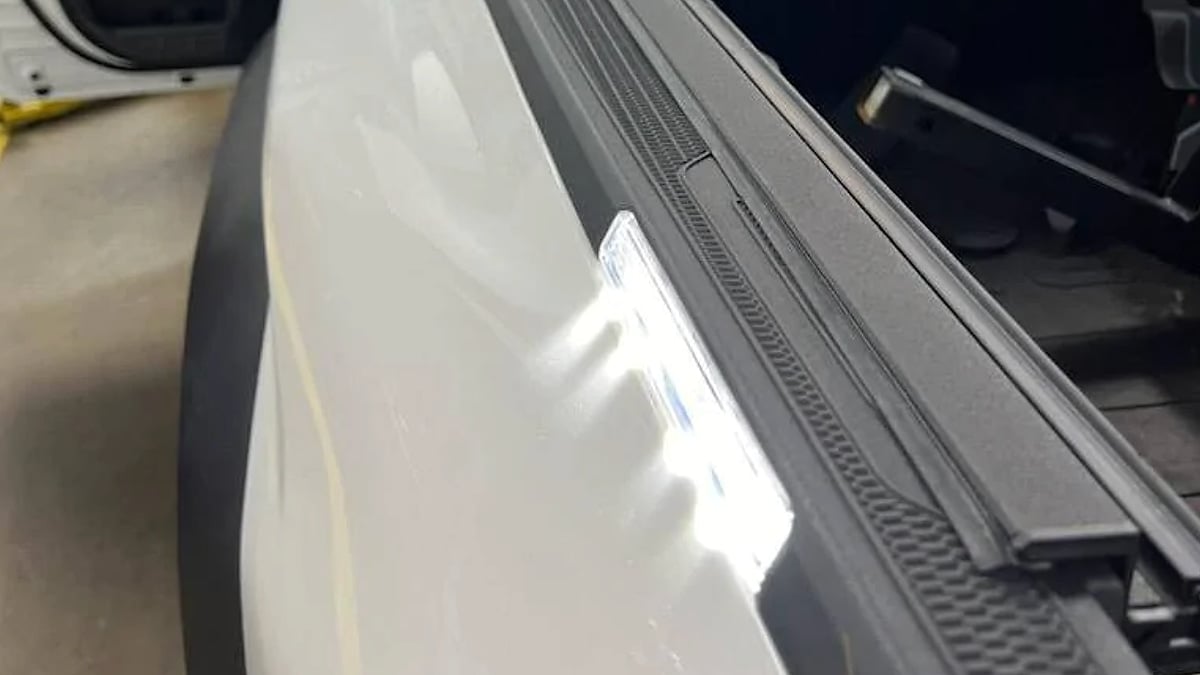 Side view of a Tacoma Trailhunter in service bay for inspection of damaged LED bed rail caps and moisture-related electrical system diagnosis