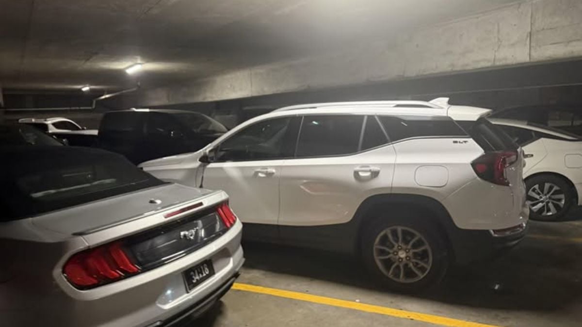 Several silver and white vehicles parked in a dimly lit indoor parking garage, with a partial rear view of what appears to be a Ford Mustang showing its distinctive taillights in the foreground.
