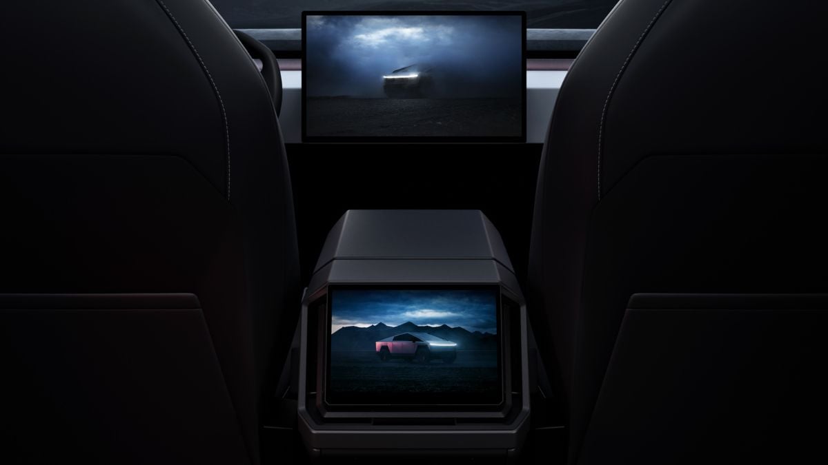 View from inside of a Tesla Cybertruck showing two screens displaying a futuristic vehicle against a moody, cloudy backdrop. The scene conveys a high-tech, innovative feel.